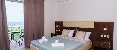 A bedroom with a bed, nightstands, a wooden ceiling, and a view of the sea through a window.