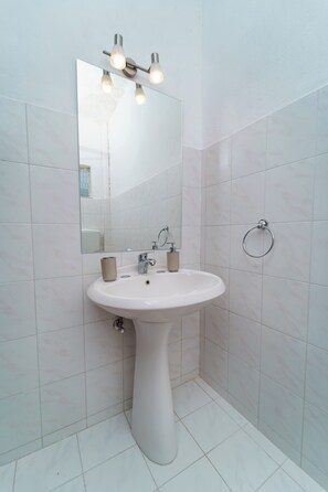 A bathroom with a pedestal sink, a mirror, and a towel ring.