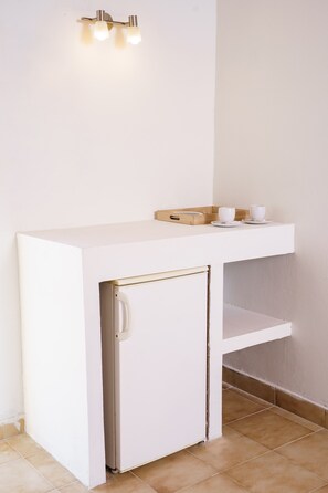 Une petite cuisine blanche comprenant un petit réfrigérateur, un plan de travail et un plateau avec des tasses.