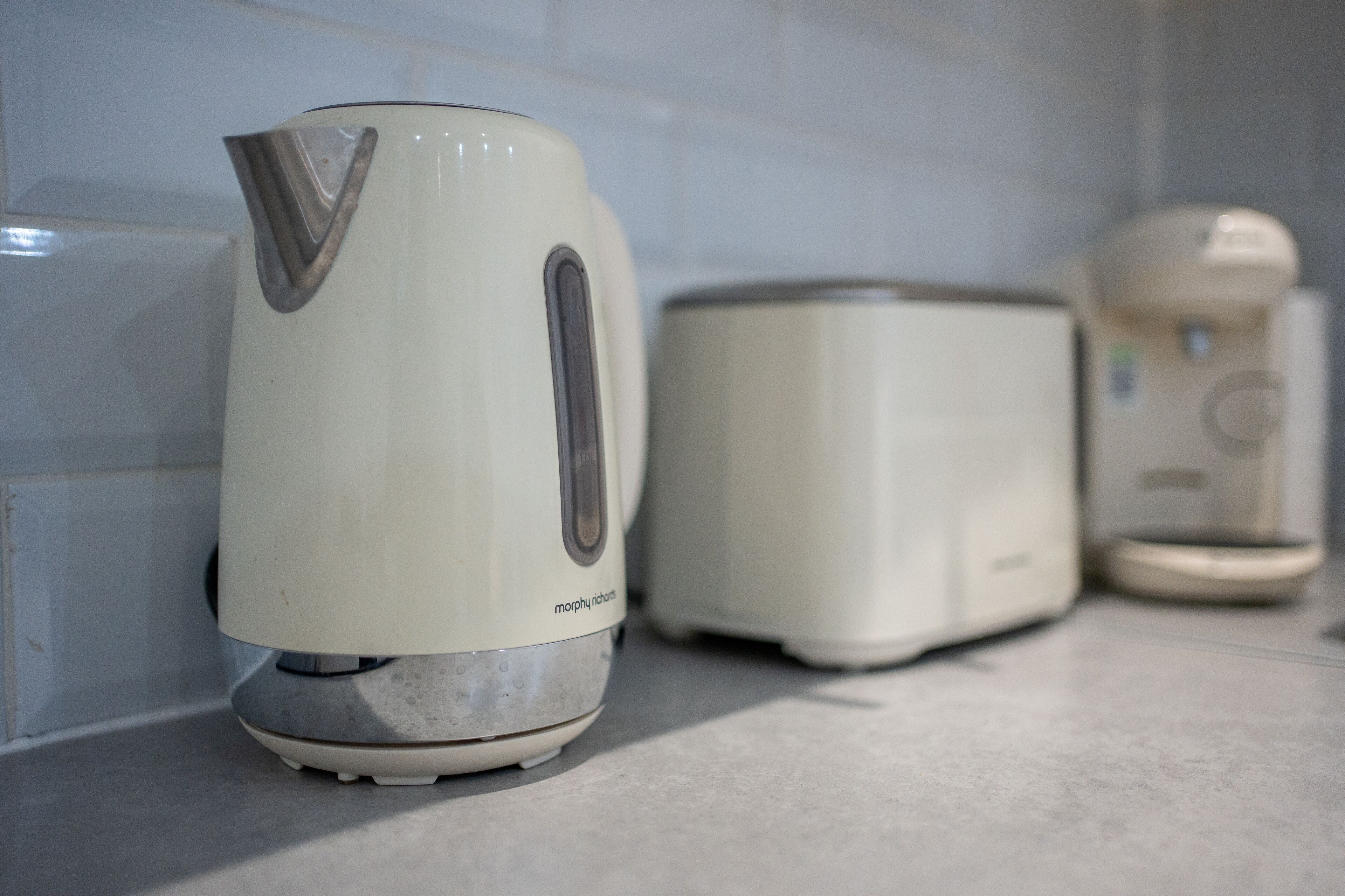 Una cocina con una tetera blanca, un tostador y una cafetera sobre la encimera.