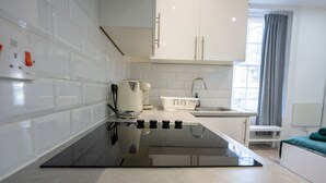 Une cuisine moderne avec des meubles blancs, une plaque de cuisson à induction noire, une bouilloire et un évier avec un robinet.