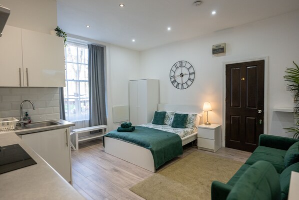 Une chambre à coucher moderne et bien éclairée, avec un lit, une table de chevet et une horloge au mur.