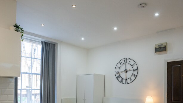 Une chambre à coucher moderne avec un lit, une table de chevet et une horloge murale.