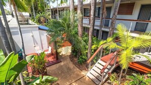 Un patio de hotel con sendero de concreto, palmeras y una escalera que lleva a un balcón.