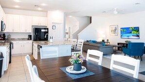 Een moderne keuken met witte kasten, een centraal eiland en een eethoek met een houten tafel en stoelen.