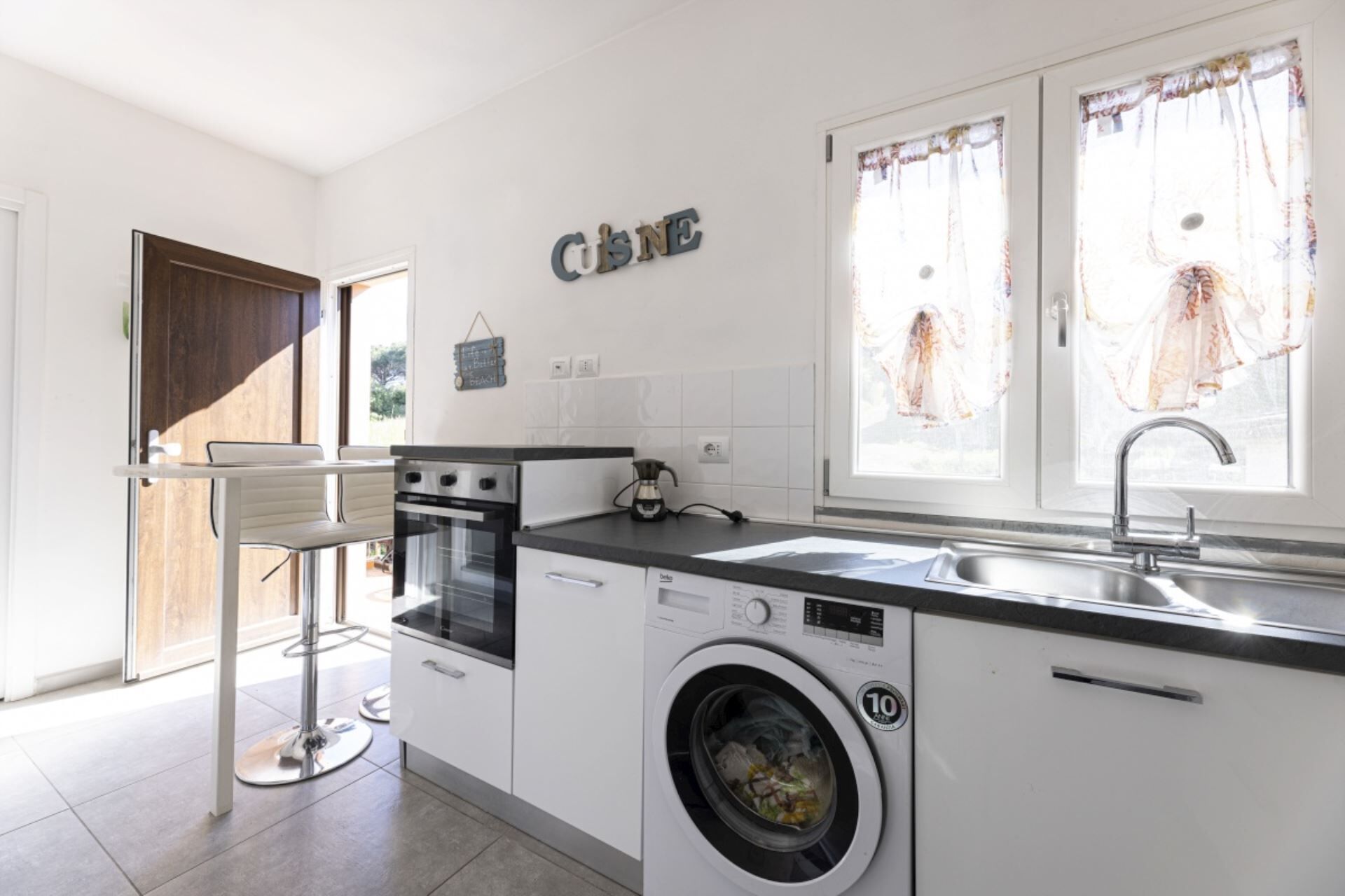 A modern kitchen with a washing machine, a coffee maker, and a sink.