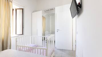 Una camera da letto con una culla, un letto, un armadio, una televisione a muro e una porta che dà su un'altra stanza.