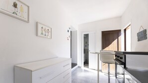 A modern kitchen with white cabinetry, a stainless steel range hood, and a small dining area with a bar stool. - Casetta Ginevra Country & Modern (Portoferraio)