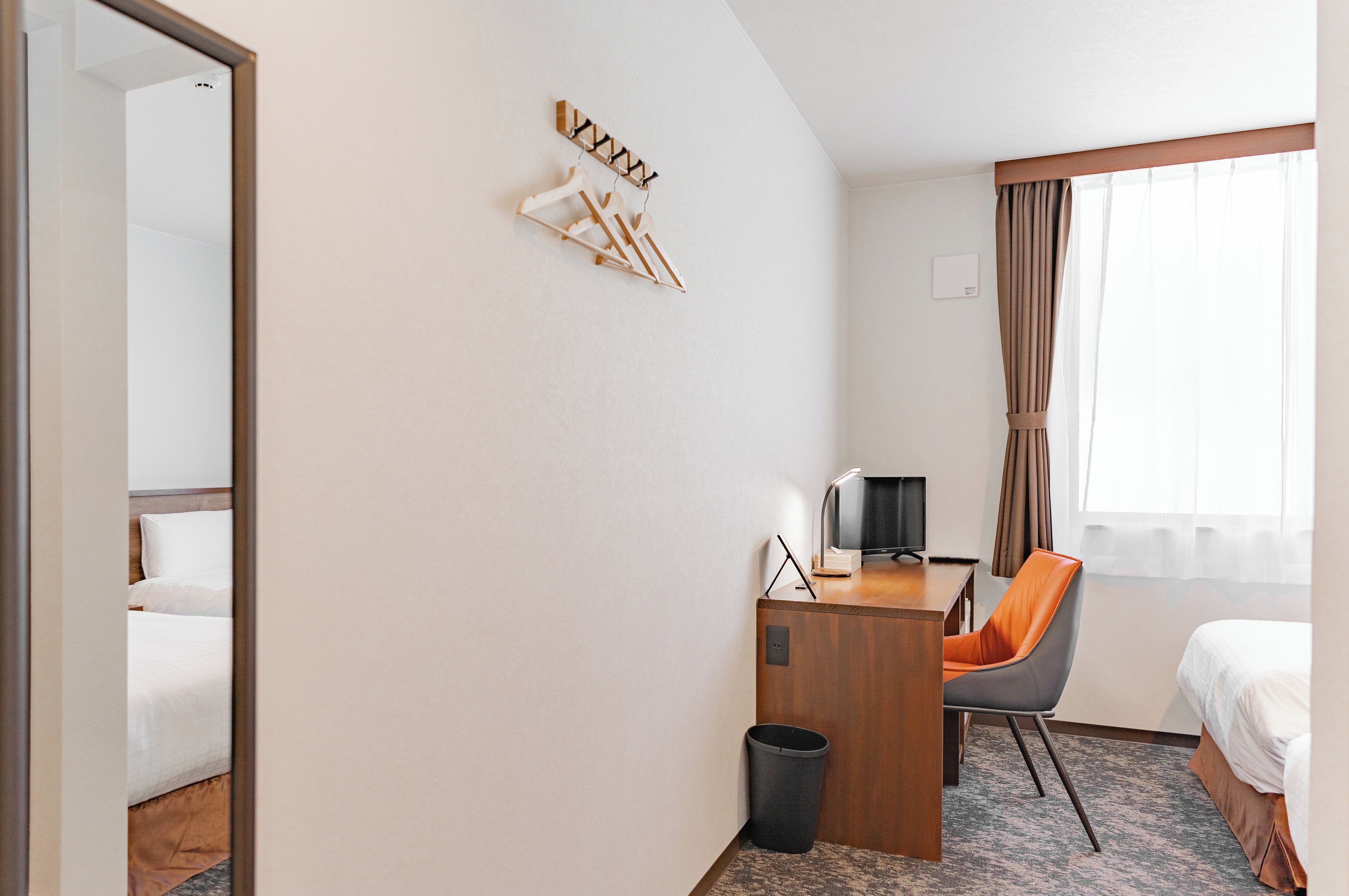 A hotel room with a bed, a desk with a chair, a TV, and a window with curtains.