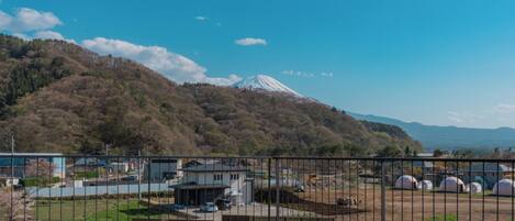 A view of a mountain with a snow-capped peak, a parking area, and a fenced enclosure with yurts.