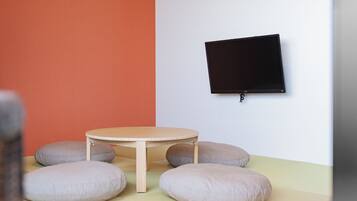 A room with a round table, four cushions, a flat-screen TV mounted on the wall, and a two-tone wall with orange and white sections.