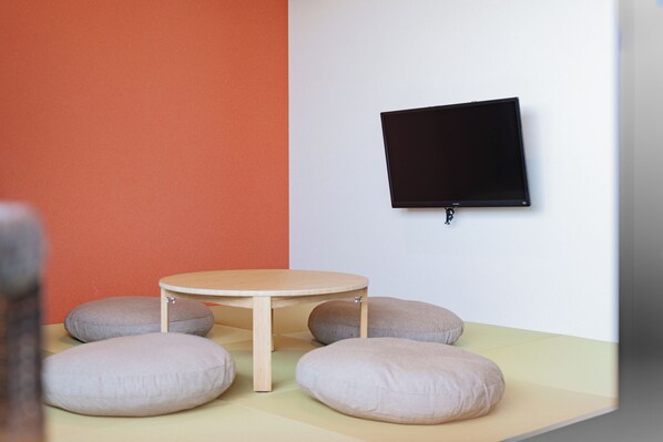 Una habitación con una mesa redonda, cuatro cojines, un televisor de pantalla plana montado en la pared y una pared bicolore con secciones naranja y blanca.