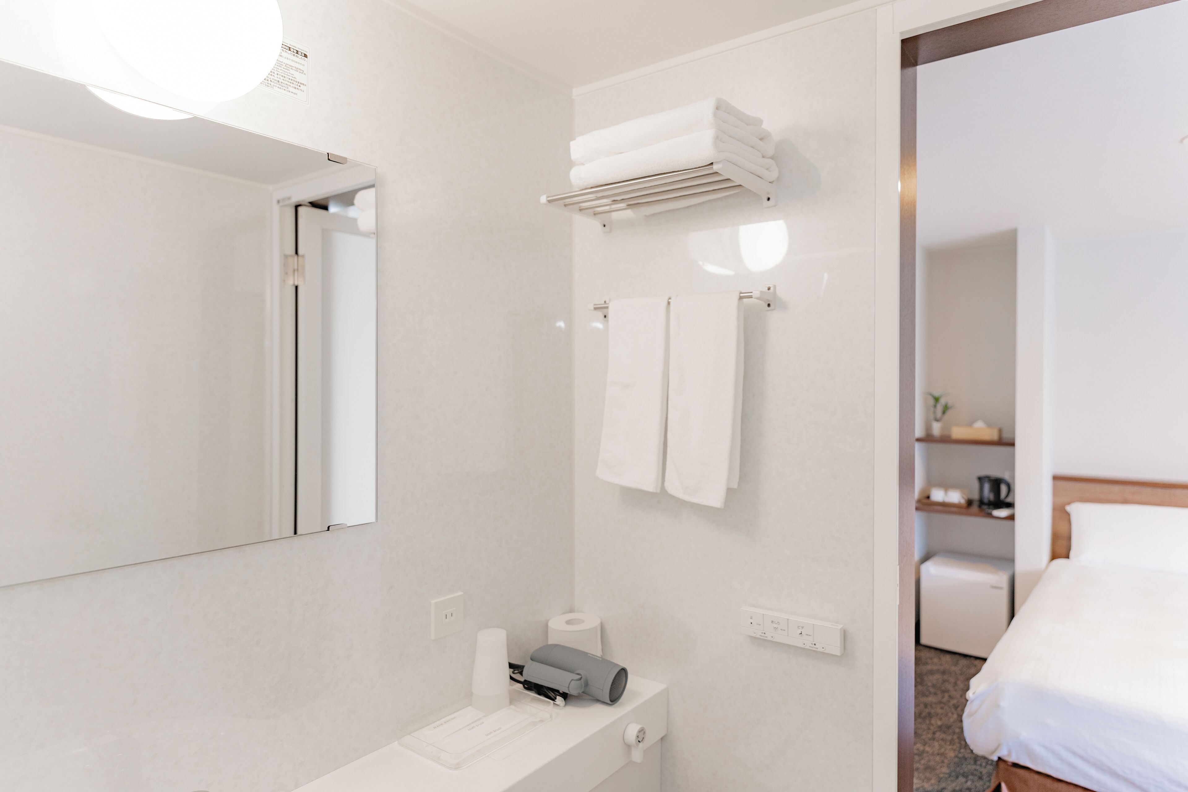 Bany d'hotel modern amb un mirall gran, un lavabo amb productes de tocador, un suport de tovalloles i un calefactor.