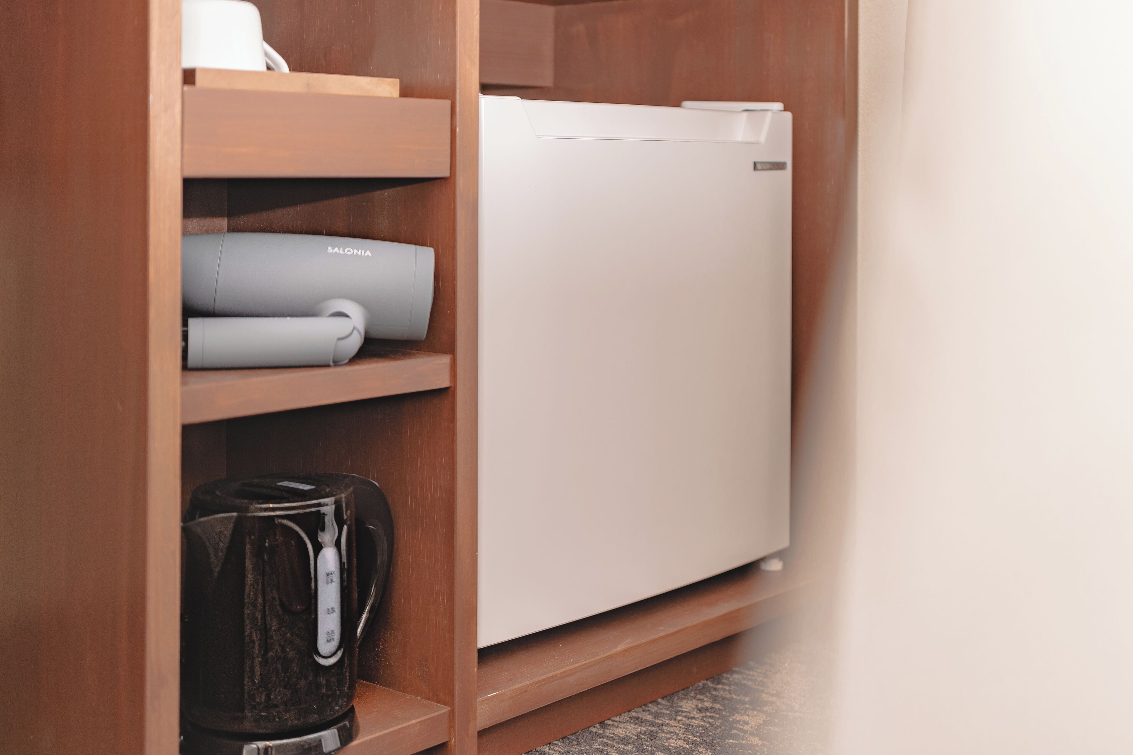 A compact kitchen with a white refrigerator, a coffee maker, and a rolled-up towel on a wooden shelf.