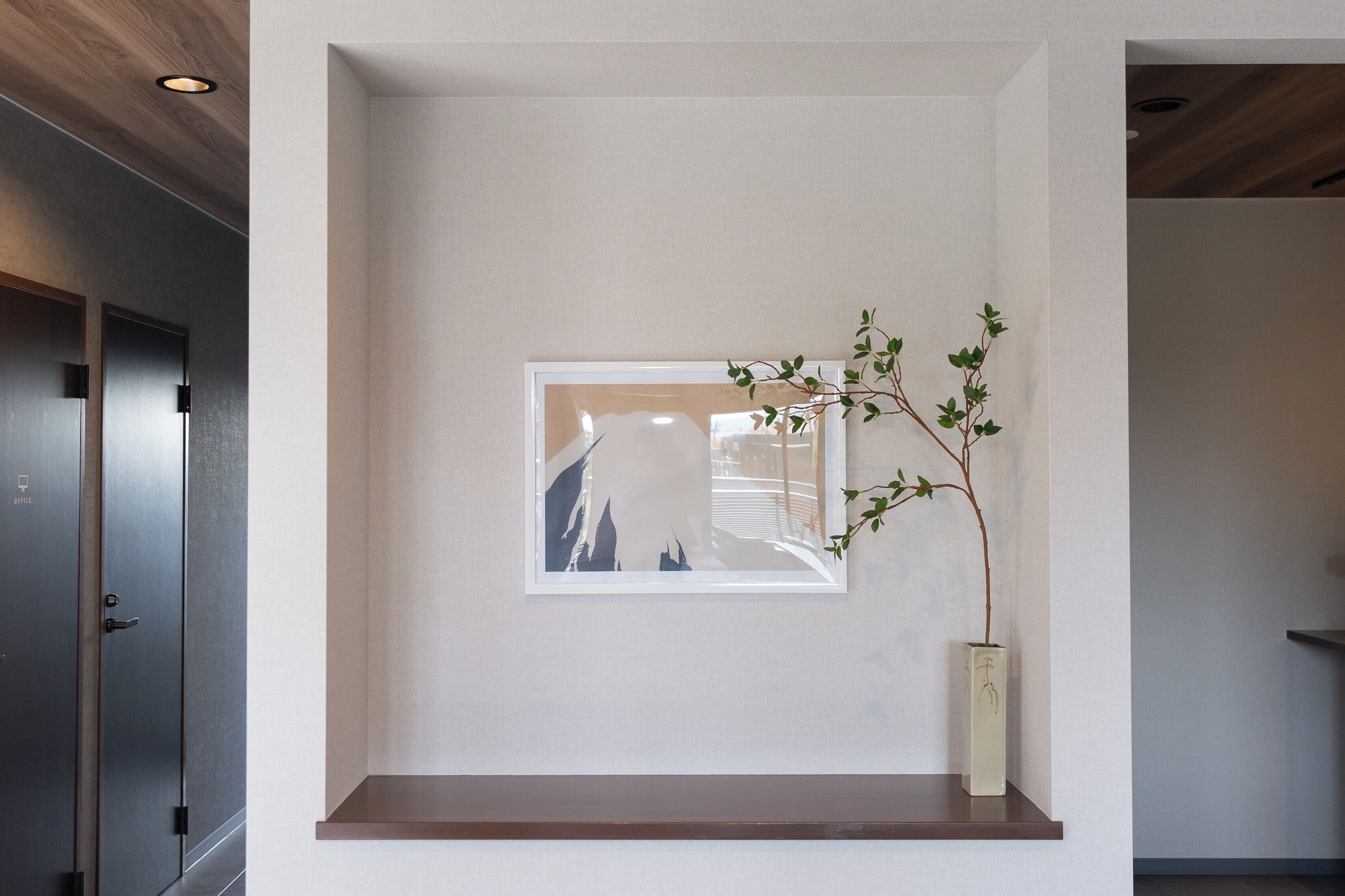 A minimalist interior with a framed artwork on the wall, a small shelf with a plant, and a door with a handle.