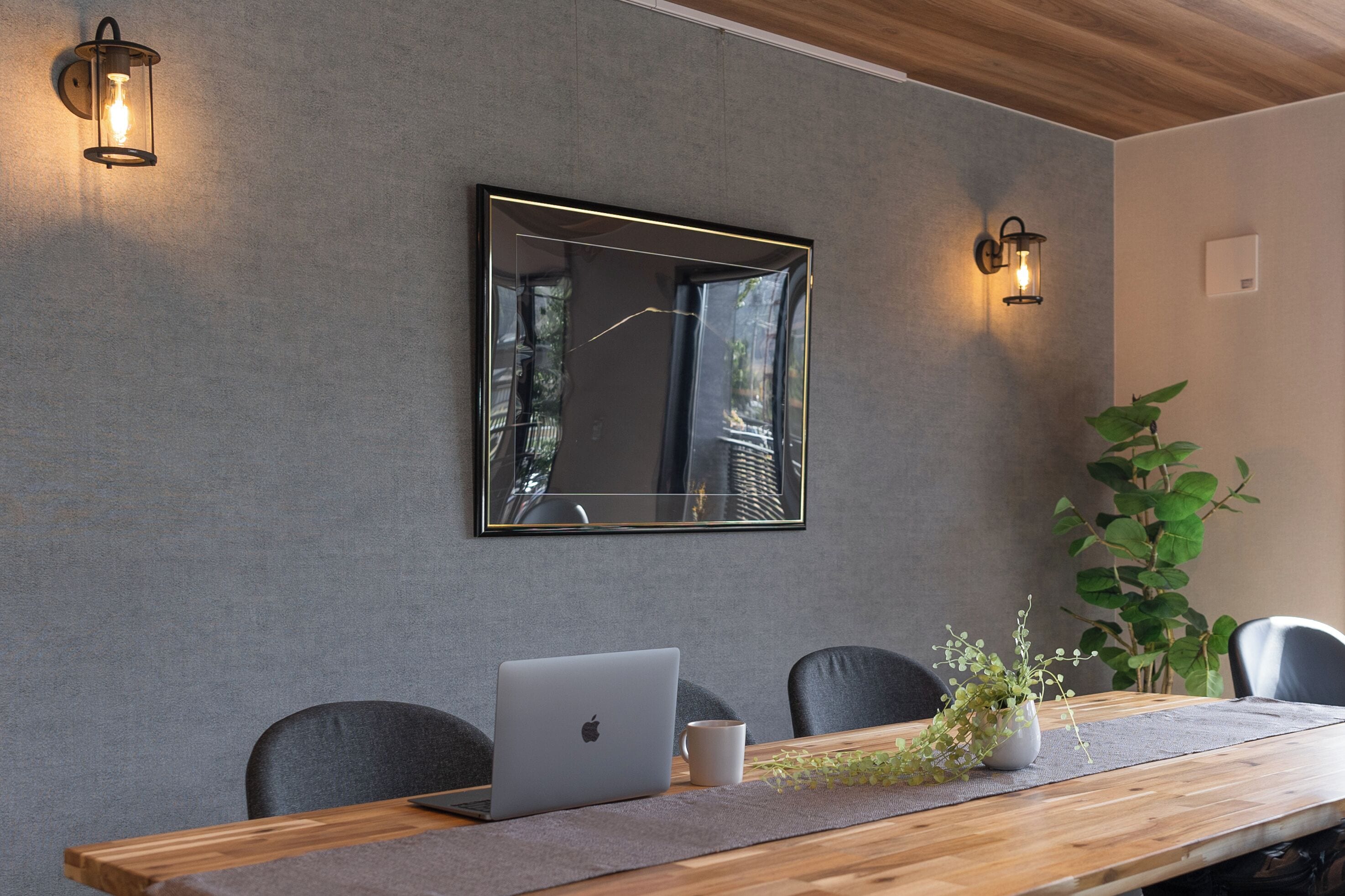 Un salón de conferencias con una mesa de madera, una computadora portátil, una taza blanca y una planta en maceta.