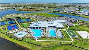 Vista aérea de una zona residencial con un edificio grande que cuenta con piscina, canchas de tenis y un parque ajardinado.