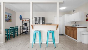 A compact kitchen with a central island, two stools, a coffee machine, and a microwave.