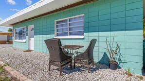 A building with teal exterior walls, a door, and a window. There are two wicker chairs and a small table outside.