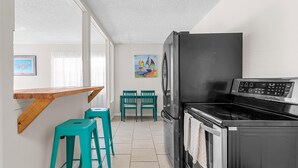 A compact kitchen with a black refrigerator, a stove, and a dining area with two green chairs.