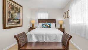 A hotel room with a large bed, two bedside tables with lamps, a wooden bench, a painting on the wall, and a window with sheer curtains.