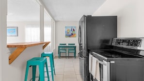 Une cuisine compacte avec un réfrigérateur noir, une cuisinière et un coin repas comprenant deux chaises vertes.