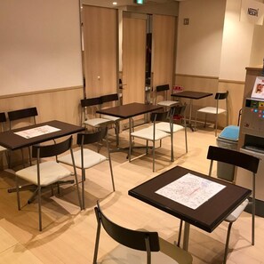 A room with tables and chairs, a vending machine, and a door.
