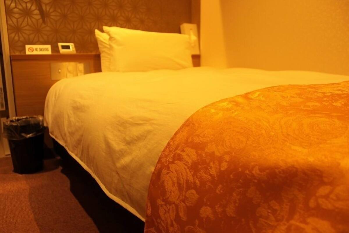 A hotel room with a bed, a nightstand, a trash bin, and a wall with a geometric pattern.