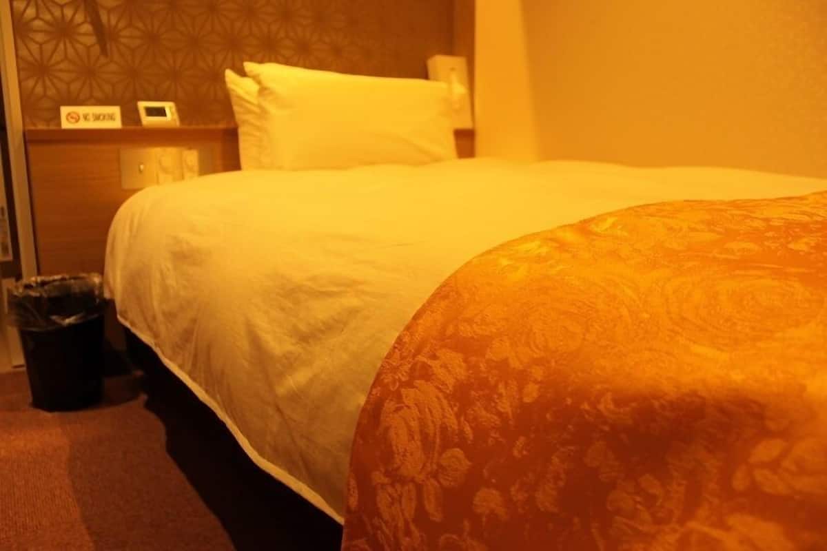 A hotel room with a bed, a nightstand, a trash bin, and a wall with a geometric pattern.