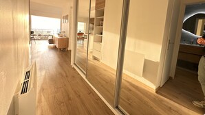 Un interior moderno con piso de madera, puerta de vidrio corredera que da a un balcón y una zona de cocina con armarios de madera.