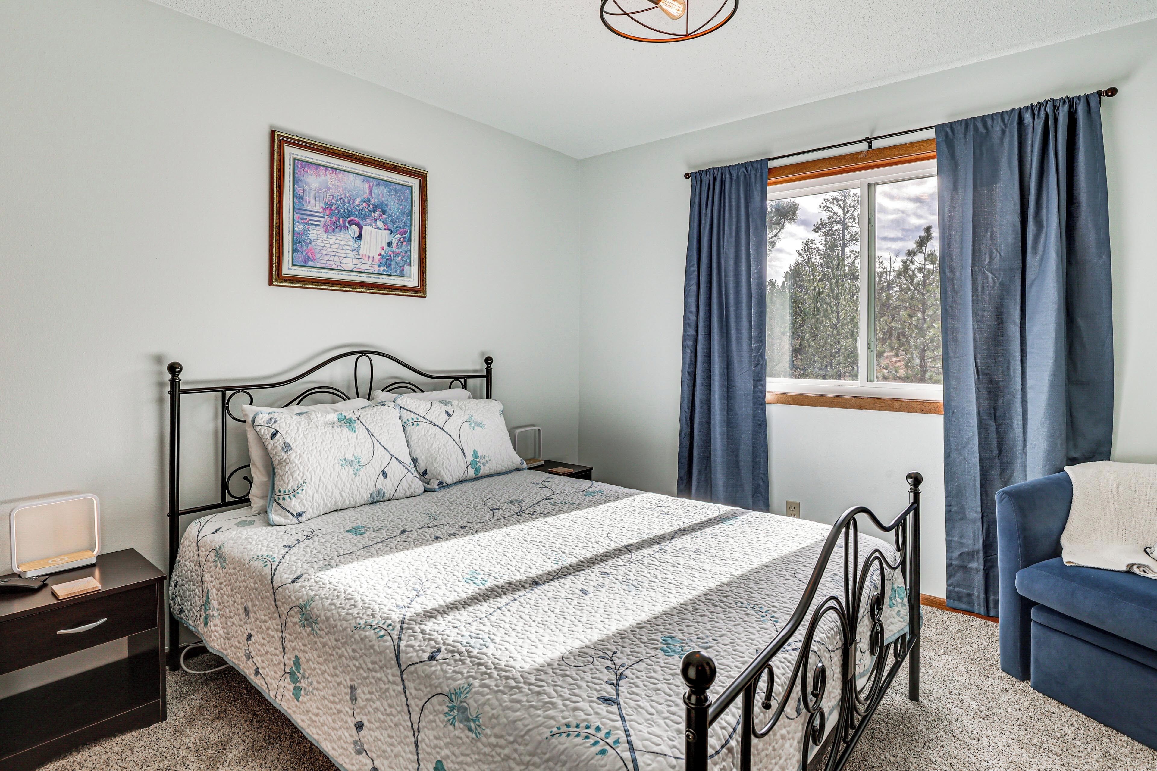 A bedroom with a bed, a bedside table, a chair, a window with curtains, and a painting on the wall.