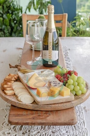 A table set with a bottle of Chandon wine, glasses, a cheese board with various cheeses, grapes, and crackers.