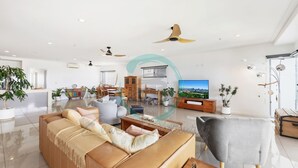 Un salón amplio con un sofá grande, un sillón gris y un televisor que muestra una vista urbana.