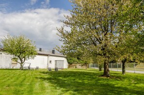 Un bâtiment blanc avec un garage, une balançoire et un grand arbre au premier plan.