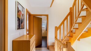 Un pasillo con una escalera de madera, un aparador de madera y una puerta que da a otra habitación.