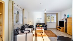 Una sala de estar moderna con sofás de cuero, una mesa de centro, un televisor sobre un soporte de madera y un ventanal con cortinas.