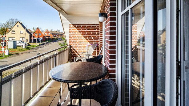 A balcony with a table and chairs, a brick wall, and a view of a street with houses.