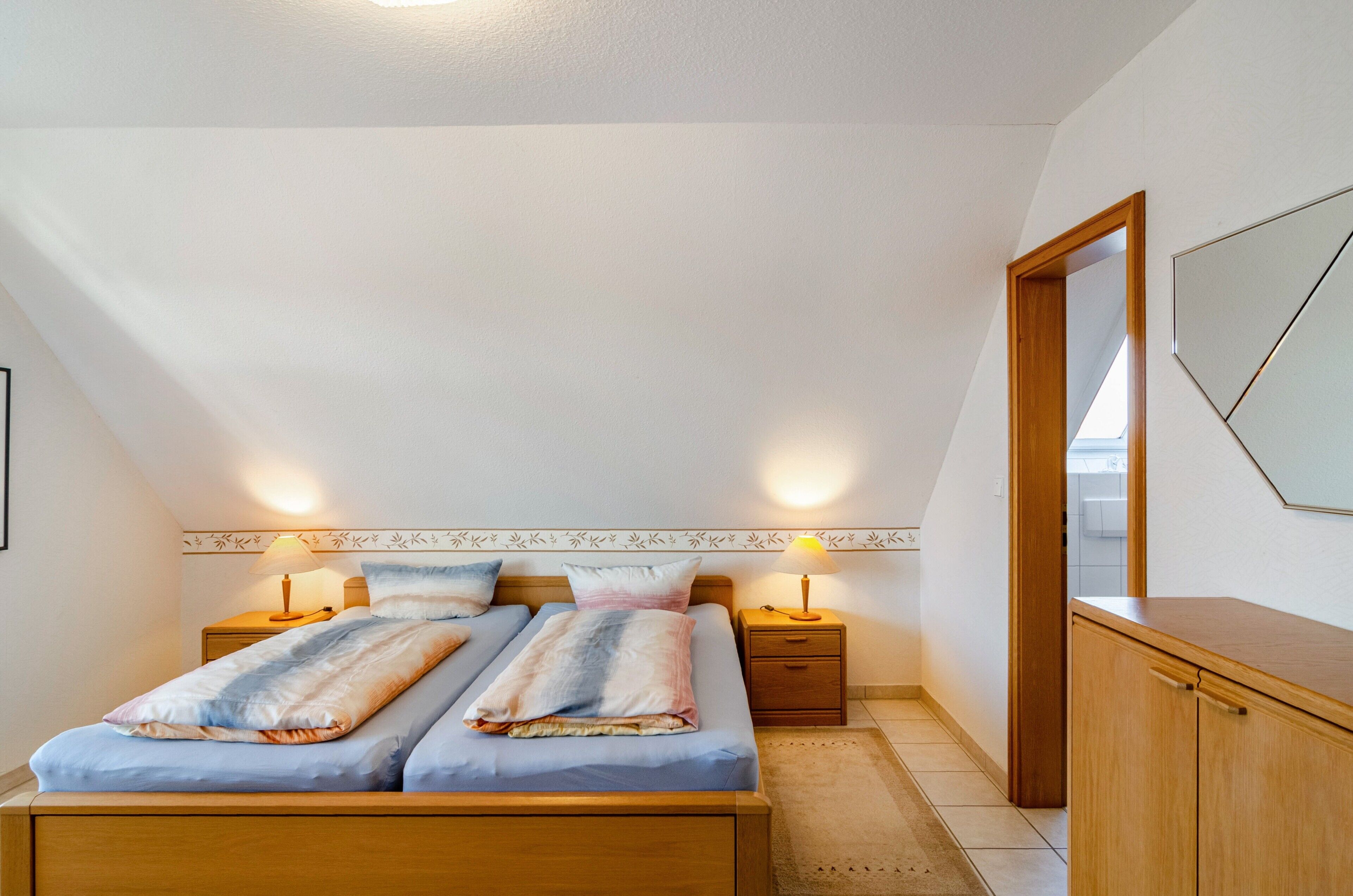 Ein Schlafzimmer mit zwei Betten, Nachttischlampen, einem Holzschrank und einem Spiegel an der Wand.