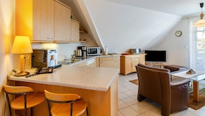 A modern kitchen with a central island, bar stools, a dining area with a sofa, and a TV.