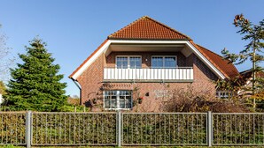 A two-story brick house with a red-tiled roof, a balcony, and a visible window.