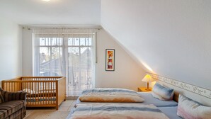A bedroom with a crib, a sofa, a bed with pillows, a nightstand with a lamp, and a framed picture on the wall.