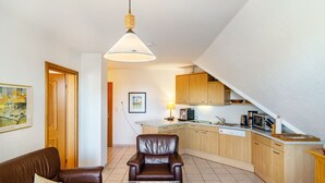 A living room with a brown leather sofa, a glass coffee table, and a brown rug. A dining area with a wooden table and chairs is visible. The kitchen has wooden cabinets and a microwave.