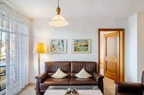 Una sala de estar con un sofá de cuero marrón, dos cuadros enmarcados, una lámpara de pie y una puerta de madera.