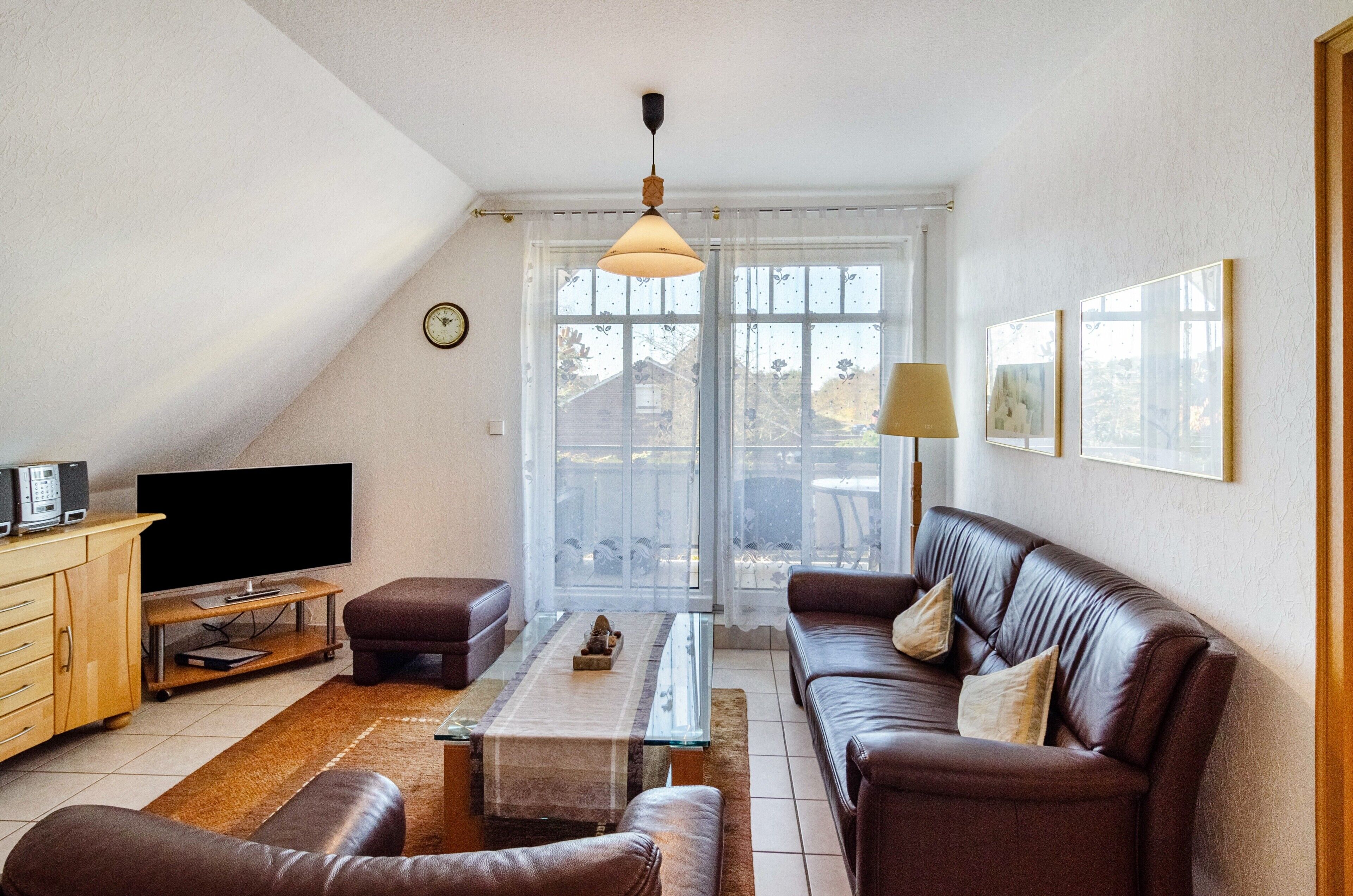 A living room with a sofa, coffee table, TV, and a view through a large window.