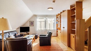 Una sala de estar con sofá, sillón, estanterías de madera, televisor y una ventana con cortinas.