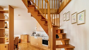 Una escalera de madera conduce a una habitación superior, una cocina con armarios de madera y un comedor.