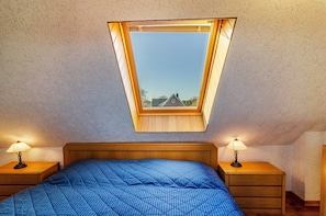 A bedroom with a sloped ceiling, a skylight, a bed with a blue quilt, and two bedside lamps. - Apartment 'Inselheide- Ferienwohnung Inselnest' with Private Terrace, Private Garden and Wi-Fi (Borkum)