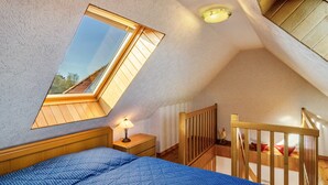 Un dormitorio con techo inclinado, tragaluz, cama de madera, mesita de noche y baranda de madera.