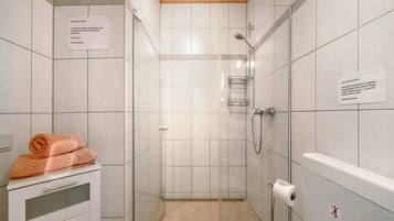 Ein kleines Badezimmer mit Fliesen, einer Dusche, einem Handtuchhalter und einem Toilettenpapierhalter.