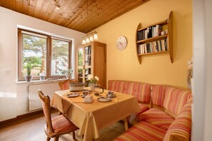 Un coin repas avec une table dressée pour deux personnes, un canapé à rayures, une bibliothèque et une horloge au mur.